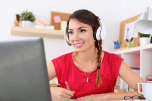 Beautiful smiling female student using online education service. Young woman looking in laptop display watching training course and listening it with headphones. Modern study technology concept